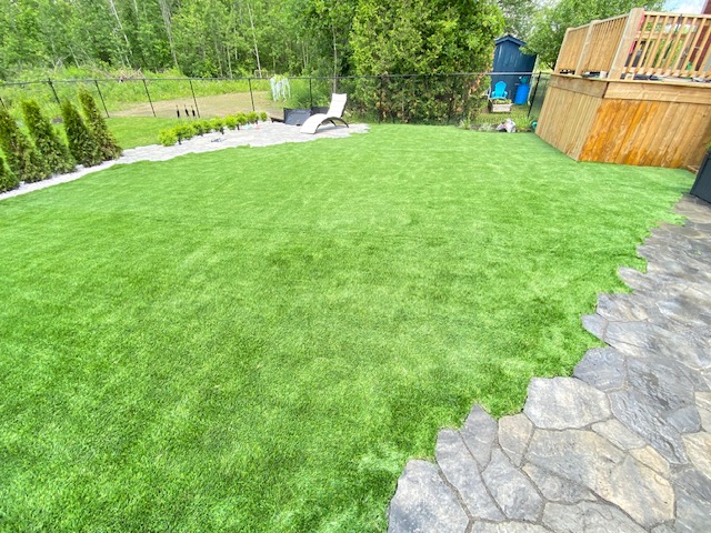 A spacious Ottawa backyard featuring synthetic grass bordered by a natural stone retaining wall and wood fencing.