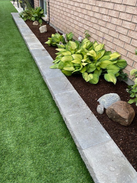A manicured synthetic lawn in Ottawa framed by natural stone and garden beds for a clean, modern appearance.