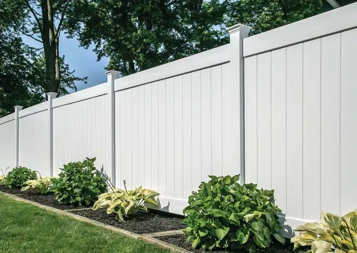 A white vinyl privacy fence in Ottawa enclosing a patio garden with flowers and interlock edging.