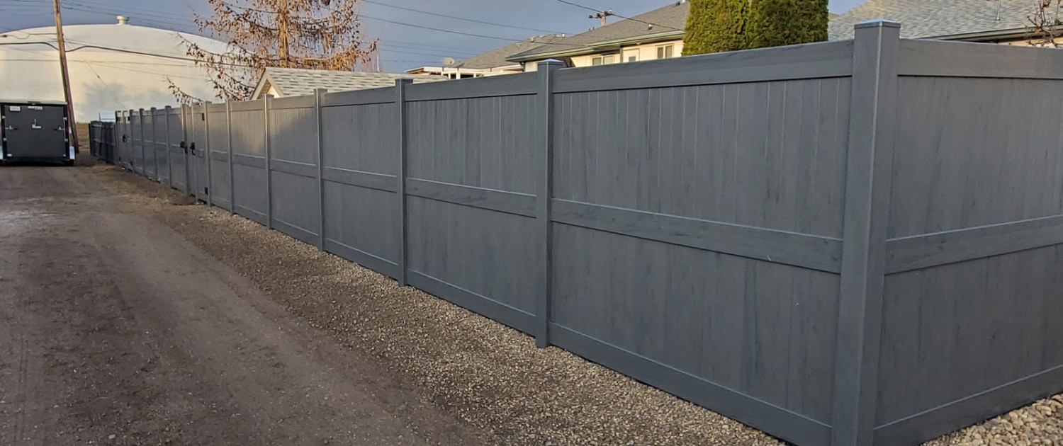 A gray-toned privacy fence in Ottawa running parallel to a paved driveway, ideal for suburban home security.